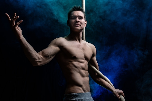 Artista di circo maschio muscoloso con cord lisse su fondo nero e affumicato