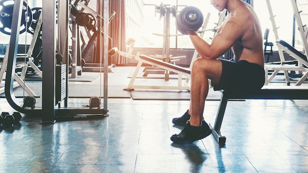 Мускулистый человек построил спортсмена, тренируясь в тренажерном зале, сидя на тяжелой атлетике