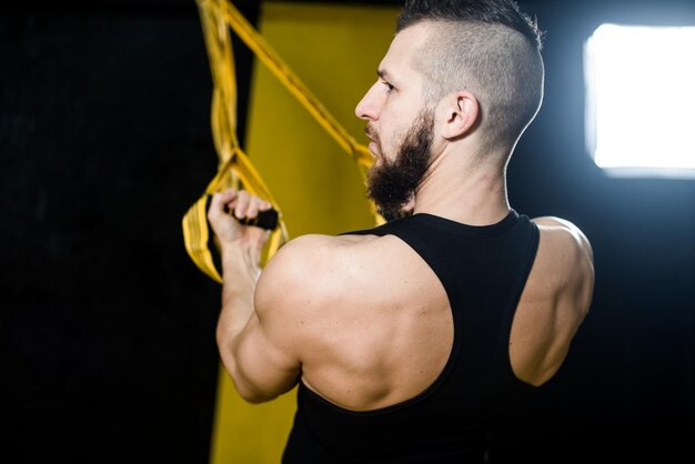 Photo muscular man does exercises with fitness straps in the gym with black and yellow interior