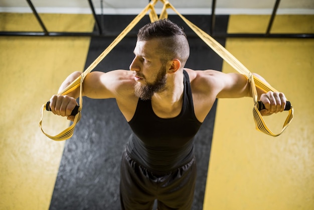 Muscular man does exercises with fitness straps in the gym with black and yellow interior