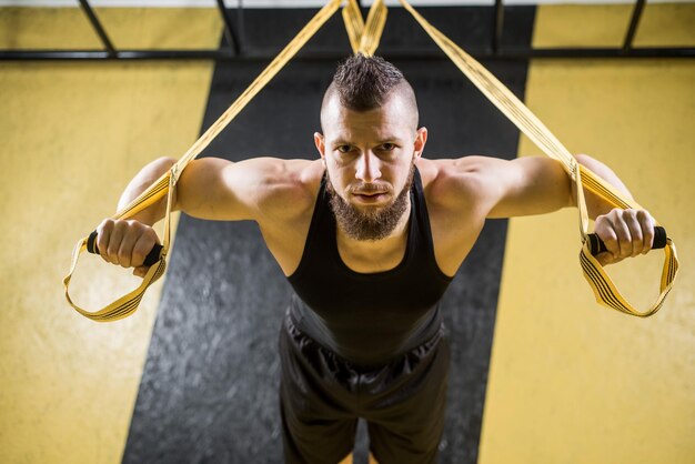 Foto l'uomo muscoloso fa esercizi con cinghie fitness in palestra con interni neri e gialli