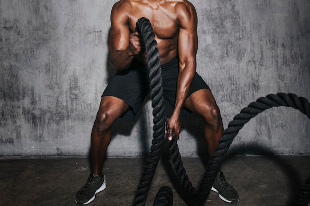 Muscular man doing a battle rope in a gym