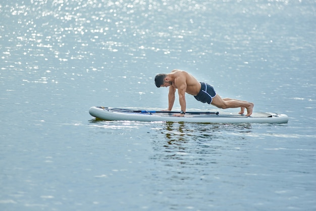 Muscular man doing emphasis on the forearm with both hands down on sup board.