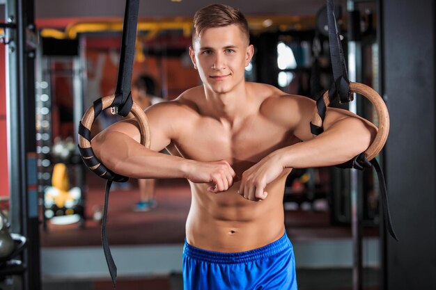Muscular man doing exercises on the rings in the gym. Emotion tension