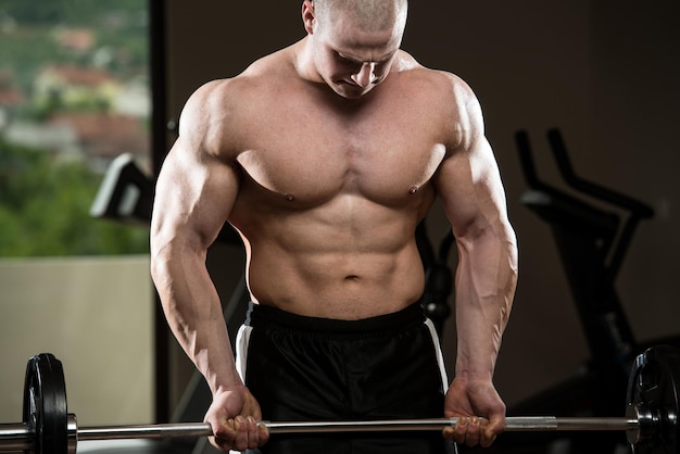 Muscular Man Doing Heavy Weight Exercise For Biceps With Barbell In Gym