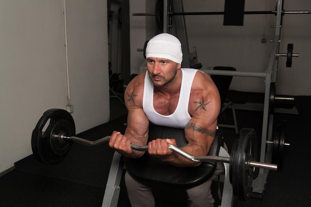 Muscular Man Doing Heavy Weight Exercise For Biceps With Barbell In Gym