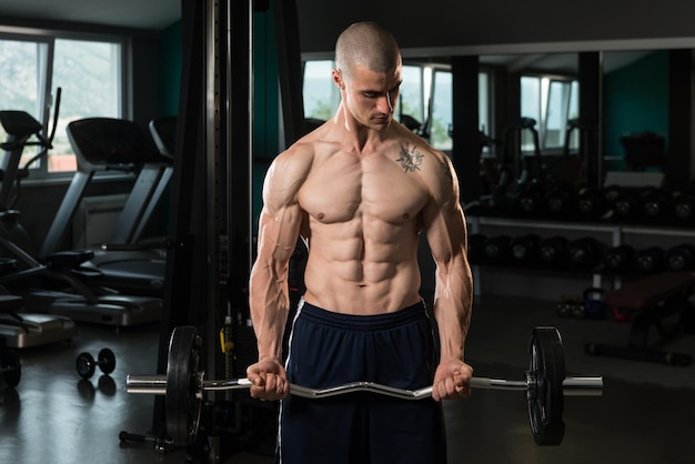 Muscular Man Doing Heavy Weight Exercise For Biceps With Barbell In Gym