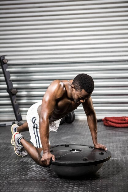 Muscular man doing push up on bosu ball at the crossfit gym