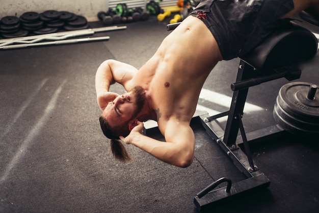 L'uomo muscolare che si esercita facendo si siede sull'esercizio