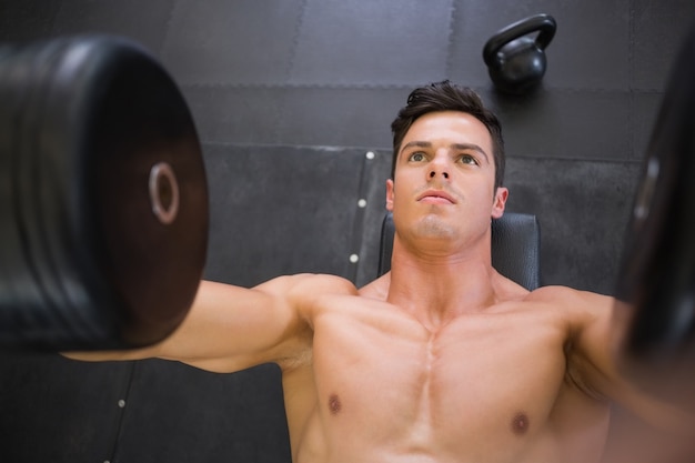 Uomo muscolare che si esercita con i dumbbells in ginnastica