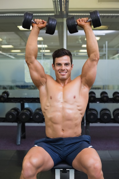 Muscular man exercising with dumbbells in gym