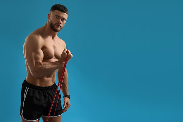 Muscular man exercising with elastic resistance band on light blue background Space for text