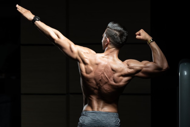 Photo muscular man flexing back muscles pose