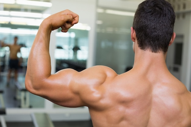 Мускулистый мужчина сгибает мышцы в тренажерном зале