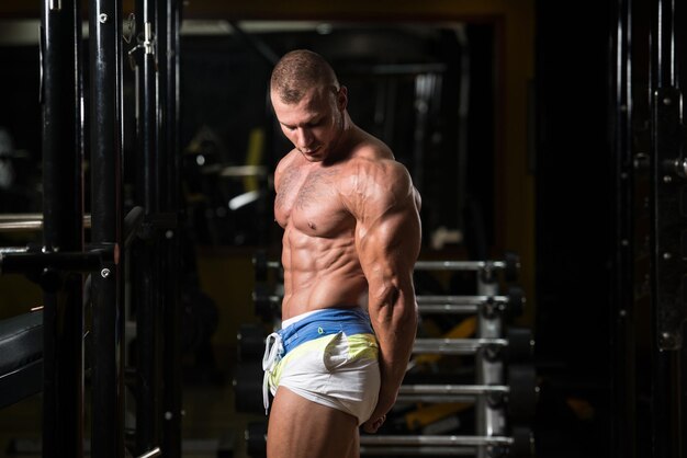 Мускулистый мужчина сгибает мышцы в тренажерном зале