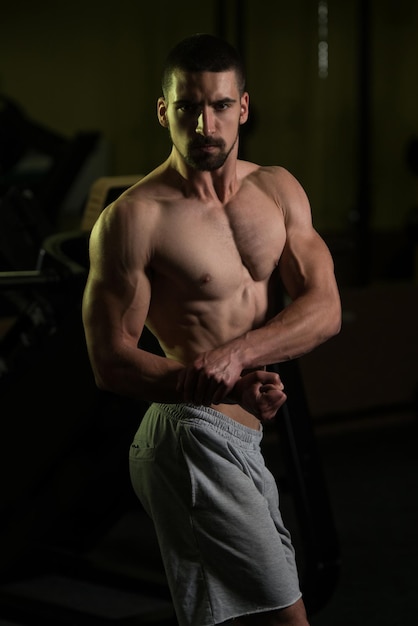 Photo muscular man flexing muscles in gym