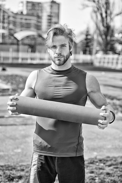 Muscular man holding yoga or fitness mat for exercise