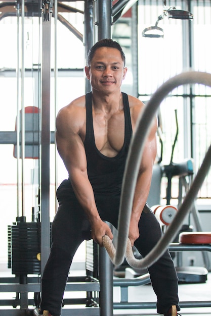 Muscular man is doing battle rope exercise