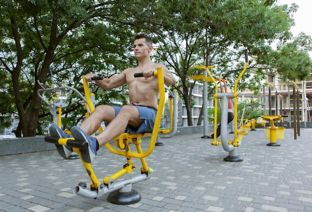 Muscular man is exercising on outdoor machines. Healthy lifestyle concept