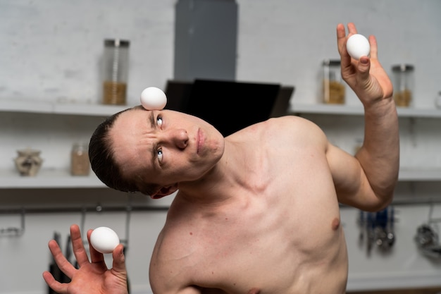 muscular man in the kitchen balancing eggs.