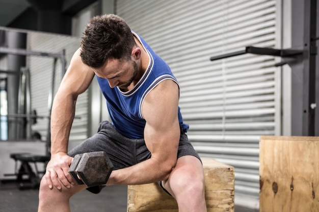 Crossfitジムで木製のブロックにダンベルを持ち上げる筋肉の男