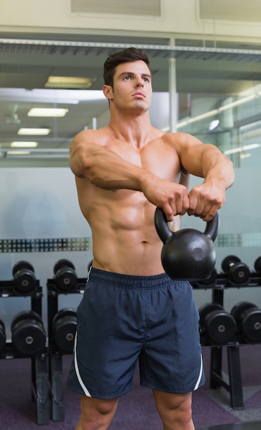 Muscular man lifting kettle bell in gym