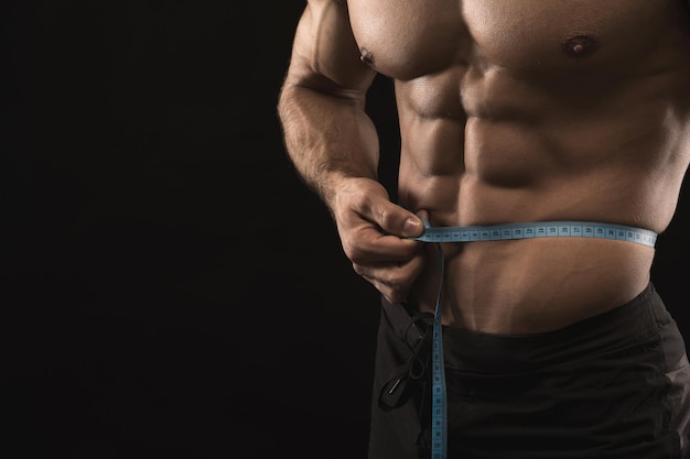 Muscular man measuring his waist closeup. Unrecognizable naked athlete with measure tape. Weightloss, healthy lifestyle, bodycare concept, copy space