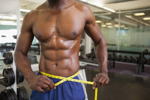 Muscular man measuring waist in gym