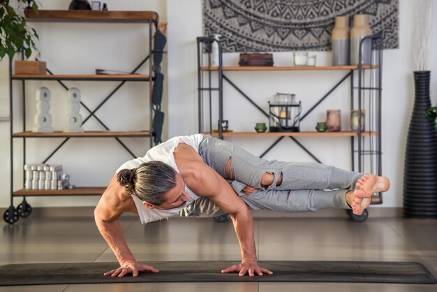 Muscular man performing side crow pose during yoga workout