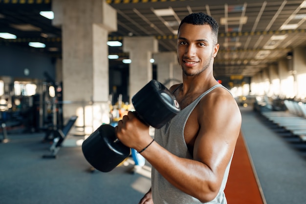 Muscular man poses with heavy dumbbell on training in gym