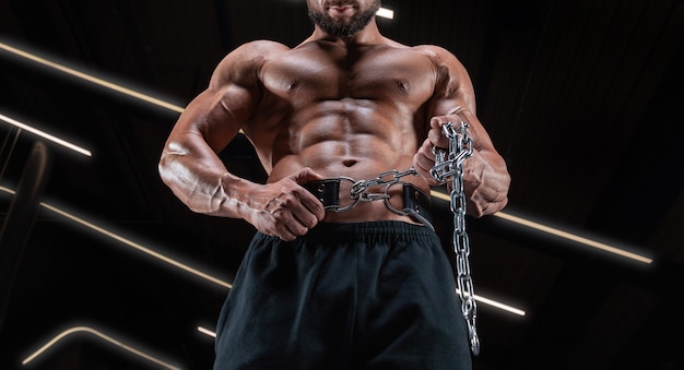 Мускулистый мужчина позирует в тренажерном зале с спортивным поясом. Концепция фитнеса.