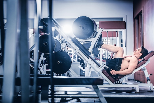 Muscular man pumping legs in machine