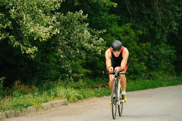 Muscular man riding his racing bike on a road through park with overgrown trees