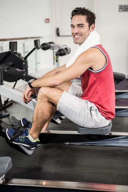 Muscular man on rowing machine smiling at the camera in the gym