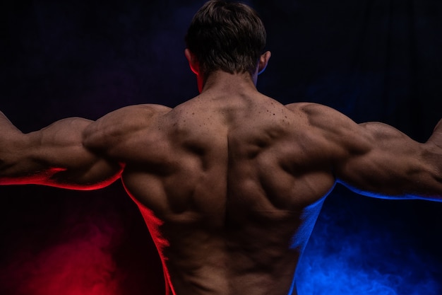 Muscular man showing muscles isolated on the black background with colored smoke