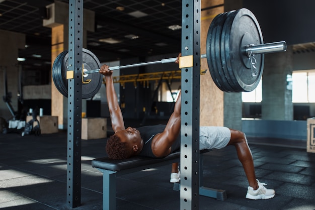 Мускулистый мужчина в спортивной одежде, упражнения со штангой на тренировке в тренажерном зале.