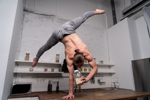 Muscular man stand on one the hand in the kitchen and cooking oatmeal concept of healthy lifestyle a...