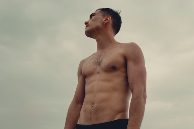 Muscular man standing on the beach in a speedo. 