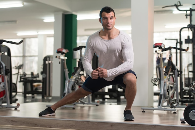 L'uomo muscoloso si allunga sul pavimento in una palestra e flette i muscoli modello di fitness bodybuilder atletico muscolare
