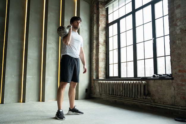 Muscular man training with kettlebells athletic man lifts a kettlebell over his head