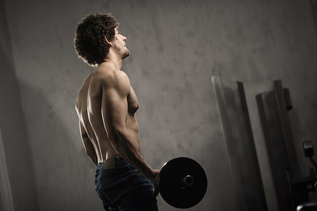 Muscular man trains biceps with barbell in the gym, hand training