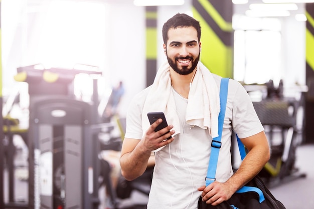 Muscular man walking in the gym holding smartphone