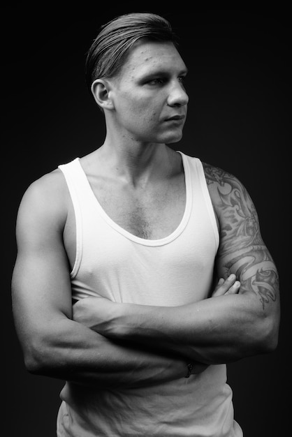 Muscular man wearing white tank top against black wall