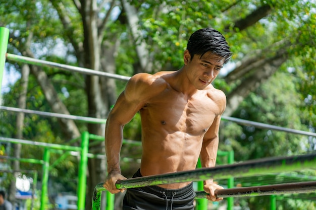 Мускулистый мужчина, который делает подтягивания, чтобы проработать мышцы бицепса и трицепса, тренируясь на свежем воздухе в парке.