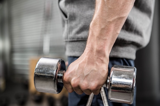 Muscular man with grey jumper holding dumbbell at the gym