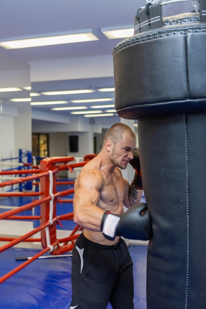 Muscular man with a naked torso in boxing gloves boxing a punching bag