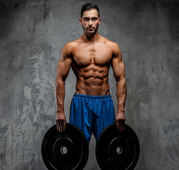 Muscular man with naked torso holding weights. Grey background