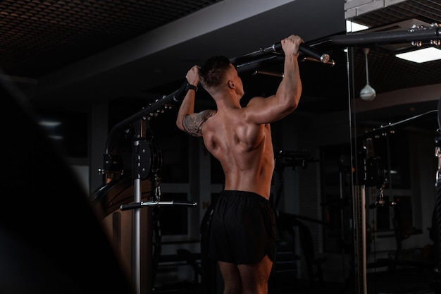 Мускулистый мужчина с голым торсом подтягивается в спортзале. Здоровый образ жизни и спорт