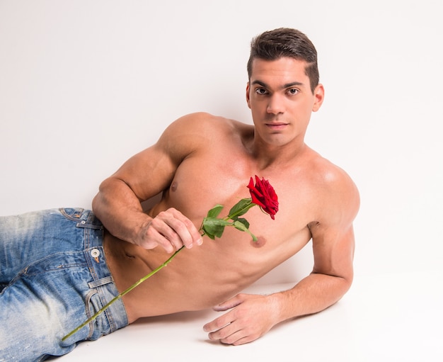 Muscular man with perfect torso is lying with rose.