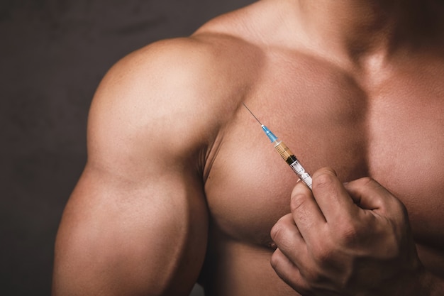 Muscular man with a syringe in his hand. Concept of a strength workout and anabolic steroids usage.